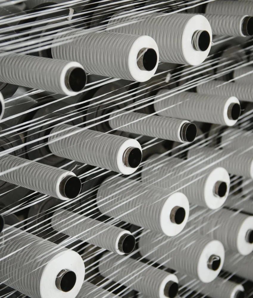 Rows of white yarn cones on a metal rack, with threads being drawn from them.